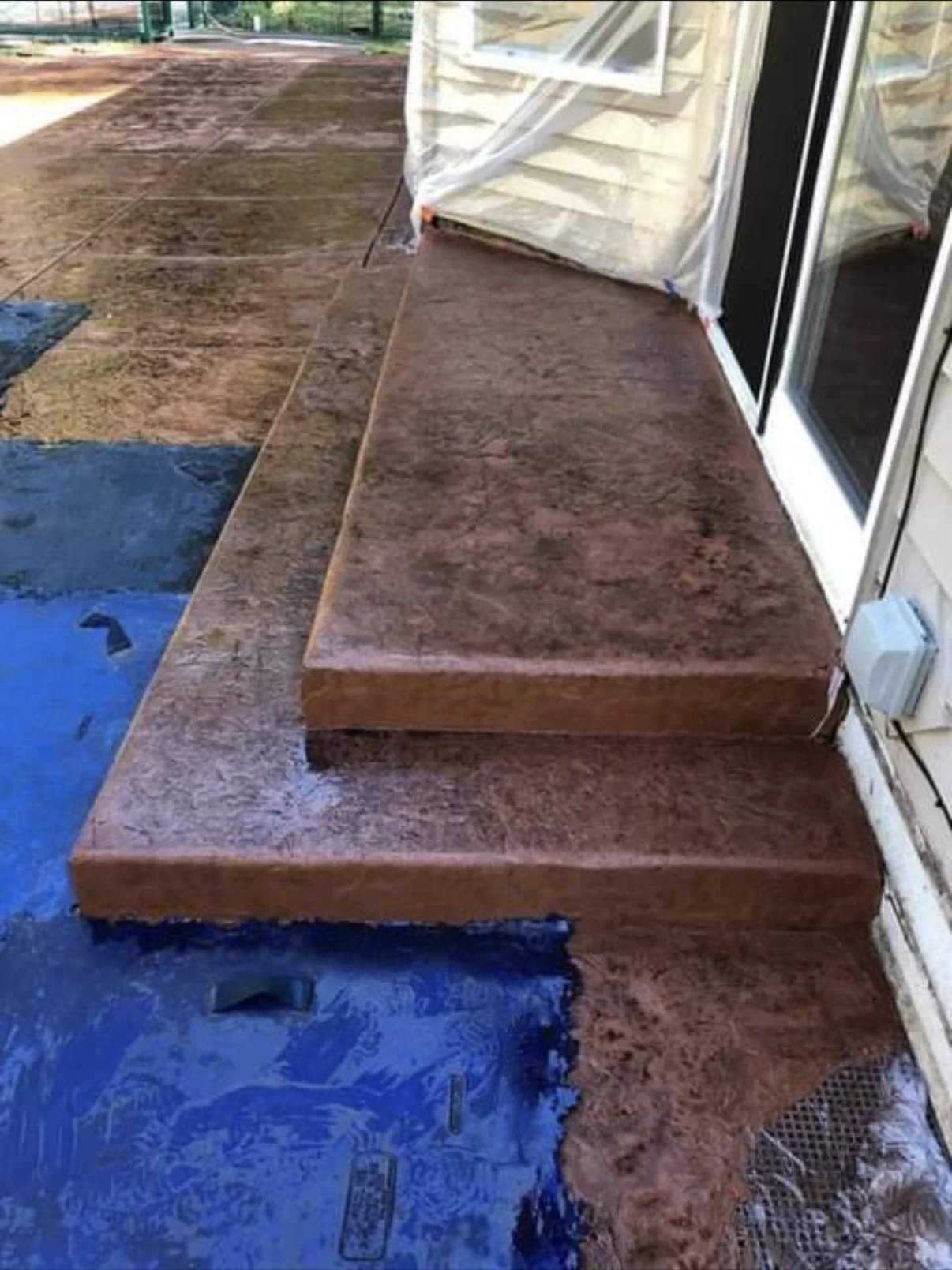 Brown stamped concrete patio with matching steps beside a sliding door